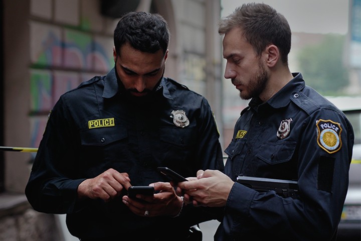 Two male police officers using smartphones while standing at crime scene